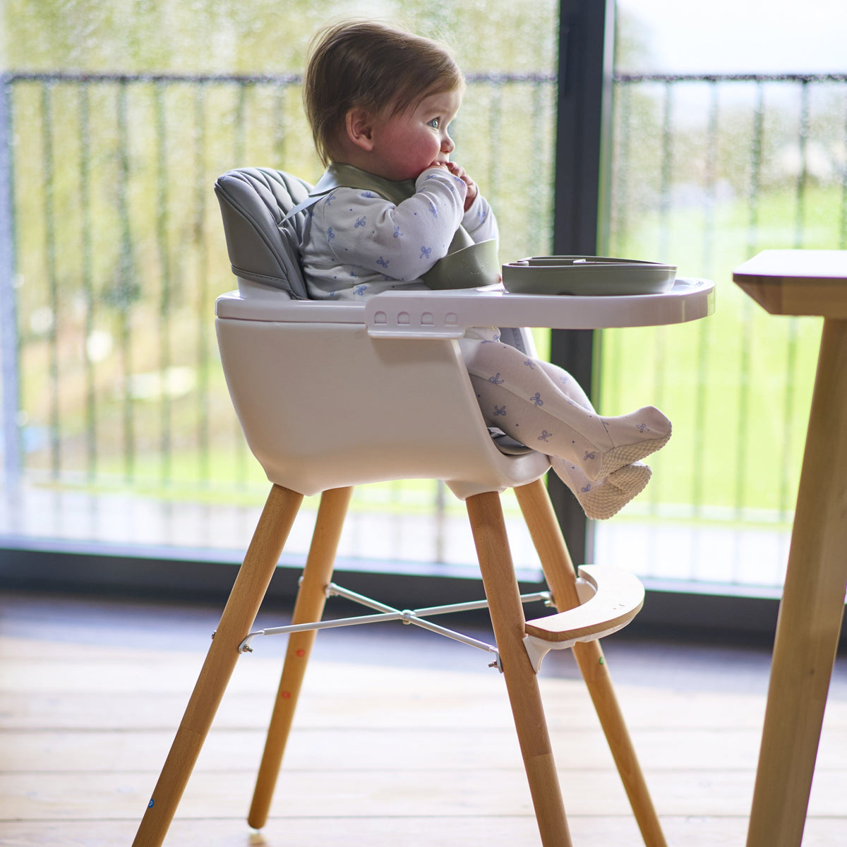 Smiling toddler in a high chair enjoying a meal at the table with natural light and toddler-safe utensils.