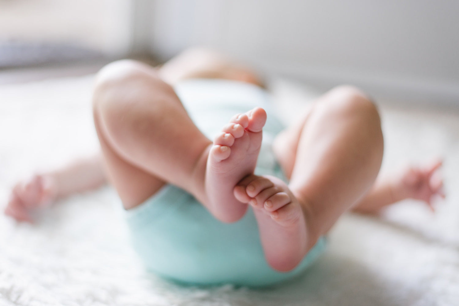 Baby lying backwards on a rug, feet showing towards the camera