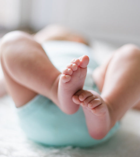 Baby lying backwards on a rug, feet showing towards the camera